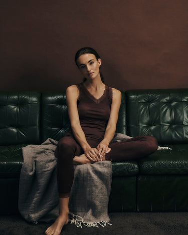 Woman sitting on a dark green leather couch in woolen lace with a plain background
